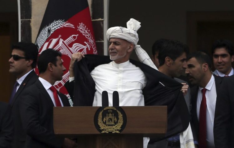 Afghan President Ashraf Ghani, center, opens his coat after a few rockets are fired during his speech at his inauguration ceremony  in Kabul on March 9. To reassure his supporters, Ghani threw open his jacket saying he wasn't even wearing a bulletproof vest. The start of Taliban prisoner releases, planned Saturday to jump-start peace talks, has been postponed. Rahmat Gul/Associated Press