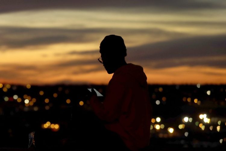 A person looks at a phone as the sun sets, in Kansas City, Mo.