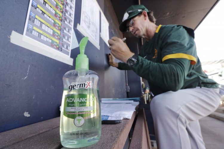 Oakland Athletics minor league manager Scott Steinmann fills out a line-up in the MLB team's dugout next to a bottle of hand sanitizer before a spring training baseball game against the Seattle Mariners  on Saturday in Peoria, Ariz. MLB is likely to cancel the rest of its spring training games and postpone openers, sources say.