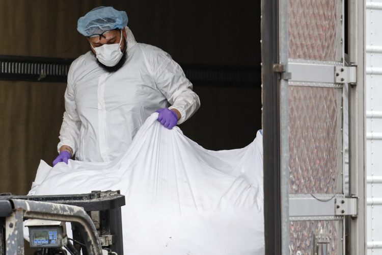 A body wrapped in plastic is loaded onto a refrigerated container truck used as a temporary morgue by medical workers wearing personal protective equipment due to COVID-19 concerns, on Tuesday at Brooklyn Hospital Center in the Brooklyn borough of New York. 