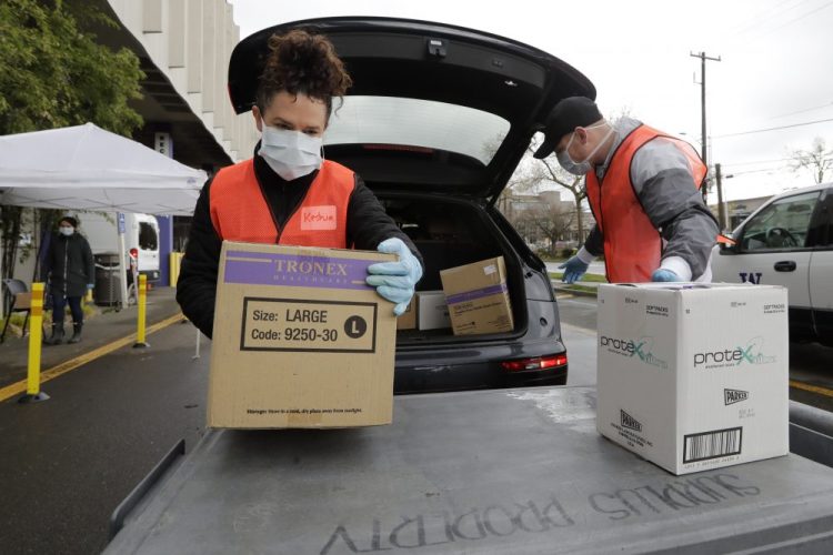 Volunteers Keshia Link, left, and Dan Peterson unload boxes of donated gloves and alcohol wipes on Tuesday from a car at a drive-up donation site for medical supplies at the University of Washington in Seattle. 