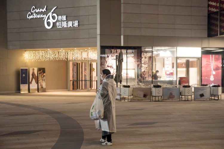 A pedestrian wearing a protective mask and rain coat stands in front of a shopping mall Feb. 12 night in Shanghai. 