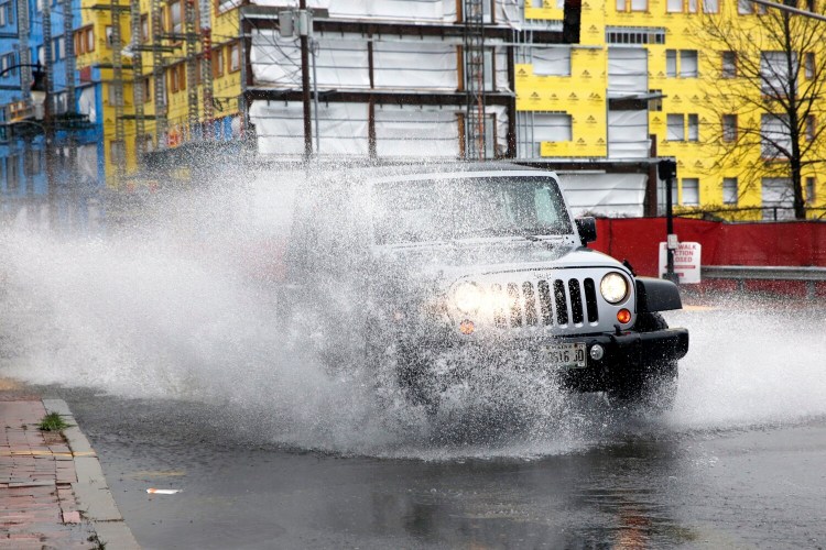 A Jeep blasts through a deep puddle at the intersection of York and High streets in Portland on Monday. 