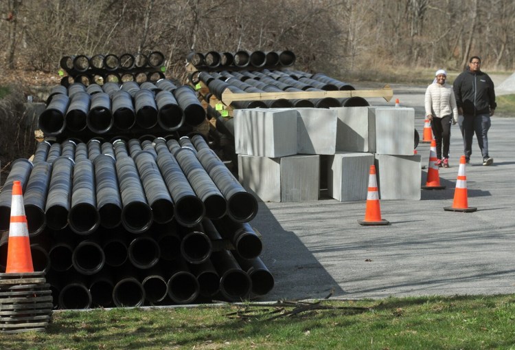 Pipes for Kennebec Water District's downtown project are stockpiled at the left, as Jonte Roussel, right, and Zainab Salih, walk by at Head of Falls in Waterville Monday. Salih is a student at Thomas College while Roussel is on staff at Thomas. 