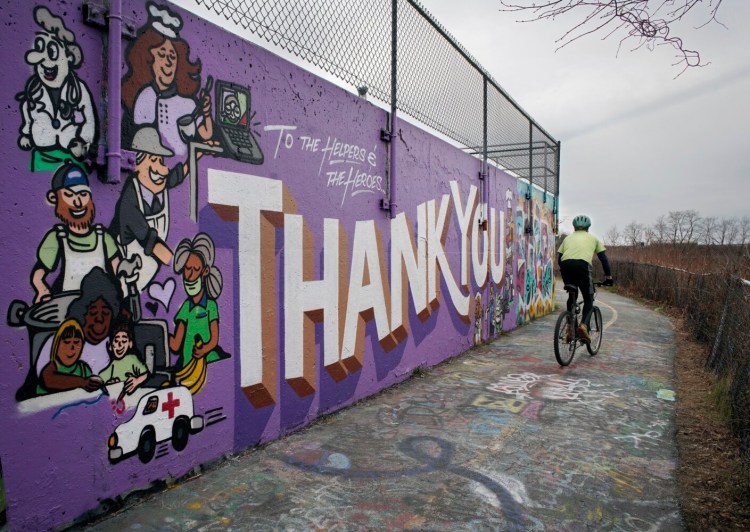 A bicyclist passes by a mural thanking the helpers and the heroes of the coronavirus pandemic on a wall near the wastewater treatment plant in Portland on Friday.