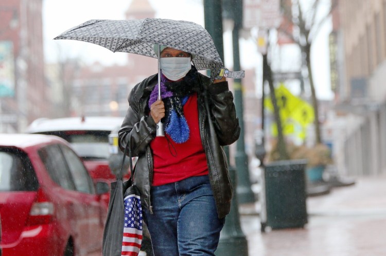 A masked woman clutches an umbrella against rain and wind while walking along Congress Street on Monday. 