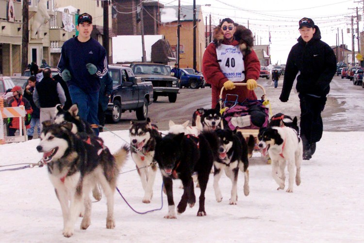 Emmitt Peters, center, is followed by his sons Emmitt Jr., left, and Emory as he drives his team up the finish chute of the Iditarod Trail Sled Dog Race in Nome, Alaska. Alaska State Troopers confirm Peters, nicknamed the "Yukon Fox," died Thursday, April 2, 2020, at his home in Ruby, Alaska. 