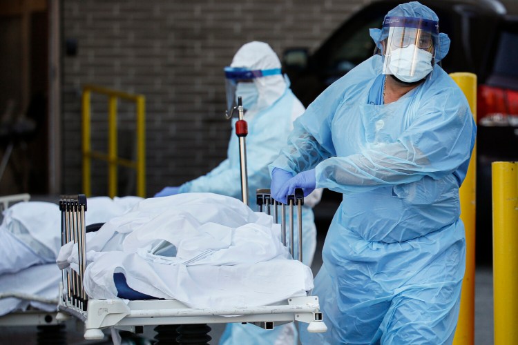 Medical workers wearing personal protective equipment wheel bodies to a refrigerated trailer serving as a makeshift morgue at Wyckoff Heights Medical Center  on Monday in the Brooklyn borough of New York. The coronavirus is taking a toll on young people as well as old. As of Wednesday, six New York residents under the age of 20, 33 people in their 20s, 118 in their 30s and 265 in their 40s had died. 