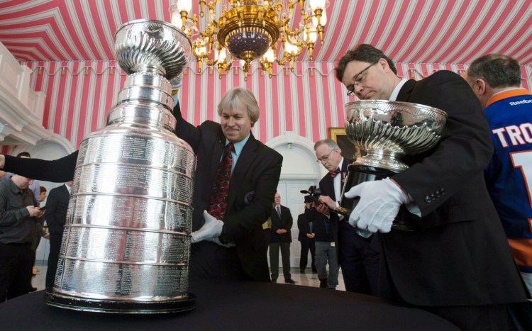 Phil Pritchard, left, picks up the Stanley Cup as Craig Campbell, right, holds the original Stanley Cup following an event commemorating the cup's 125th anniversary in 2017 at Rideau Hall in Ottawa, Ontario. The NHL is on hold, the cup is locked up inside the Hockey Hall of Fame and longtime keeper Pritchard has shed his trademark white gloves to work from home like so many others during the coronavirus pandemic.