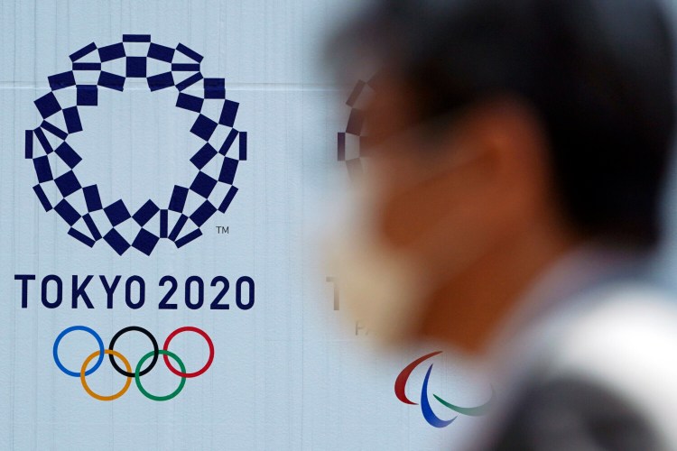 A man wearing a face mask walks near the logo of the Tokyo 2020 Olympics, in Tokyo. Tokyo Olympic organizers said Tuesday they have no “B Plan” for again rescheduling the Olympics, which were postponed until next year by the virus pandemic. 