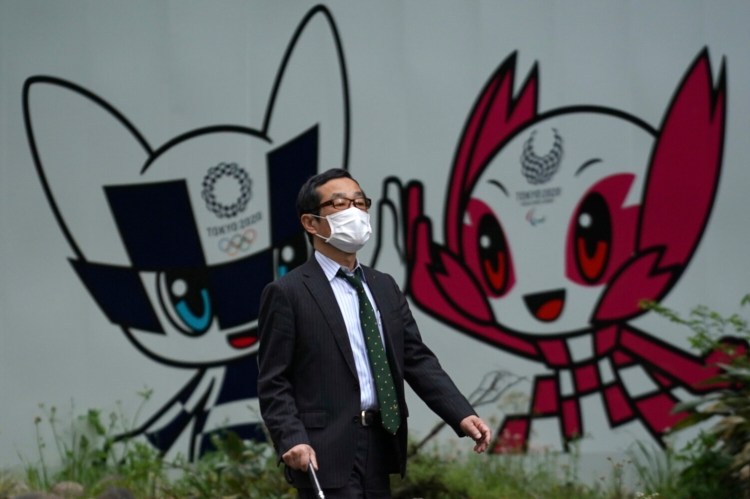 A man with a face mask walks in front of Miraitowa and Someity, mascots for the Tokyo 2020 Olympics and Paralympics at a park in Tokyo on Tuesday. 
