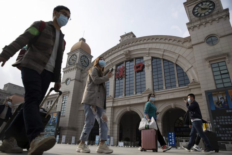 Travelers with their luggage walk past the Hankou railway station on Tuesday, the eve of its resuming outbound traffic in Wuhan, China. Starting Wednesday, residents will be allowed to once again travel in and out of the sprawling city where the  pandemic began.