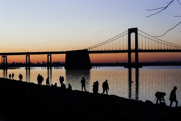 People gather to watch the sun set behind the Throgs Neck Bridge at LIttle Bay Park on Wednesday in the Queens borough of New York. While New York Gov. Andrew Cuomo said New York could be reaching a "plateau" in hospitalizations, he warned that gains are dependent on people continuing to practice social distancing. 