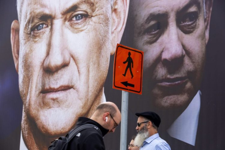 People walk past an election campaign billboard for the Blue and White party, the opposition party led by Benny Gantz, left, in Ramat Gan, Israel, in February. Prime Minister Benjamin Netanyahu of the Likud party is pictured at right. Netanyahu and Gantz announced Monday, that they have forged a deal to form an “emergency” government. 