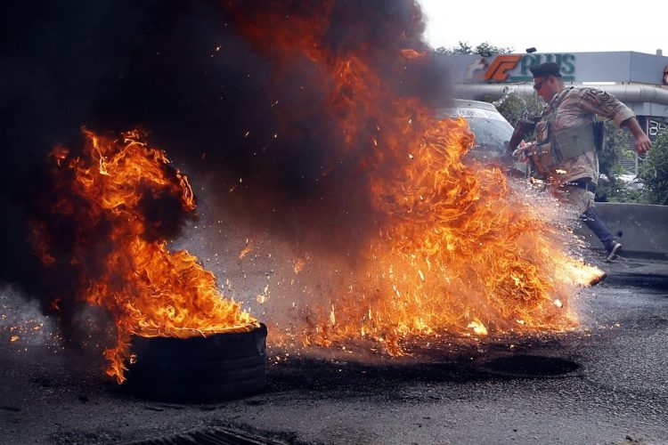Lebanese soldiers remove burning tires placed by anti-government protesters to block a road in the town of Zouk Mosbeh,  Lebanon, on Monday. 