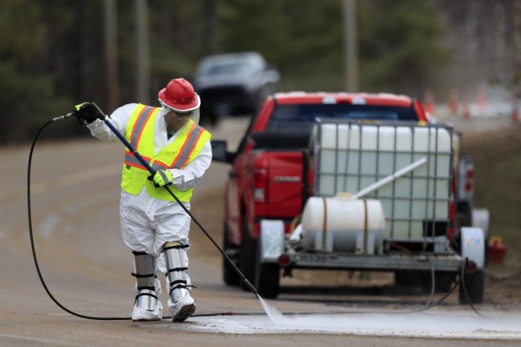 A worker wearing a hazardous material suit hoses debris off a road near the Androscoggin Mill, April 16 in Jay.