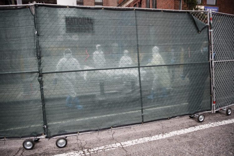 Medical workers wearing personal protective equipment due to COVID-19 concerns move a body behind a fence at The Brooklyn Hospital Center, Thursday in the Brooklyn borough of New York.