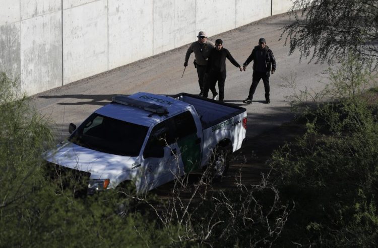 A U.S. Customs and Border Patrol agent walks with suspected immigrants caught entering the country illegally Nov. 16, 2016, along the Rio Grande in Hidalgo, Texas. The Trump administration has quietly shut down the nation's asylum system for the first time in decades amid coronavirus concerns, largely because holding people in custody is considered too dangerous.