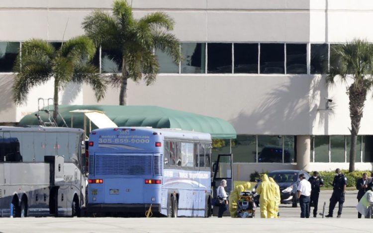 Paramedics wearing yellow protective suits to prevent the spread of the coronavirus stand at the ready as passengers who came off the cruise ship Rotterdam get off a bus to board a charter plane at Fort Lauderdale–Hollywood International Airport on Friday in Fort Lauderdale, Fla.  