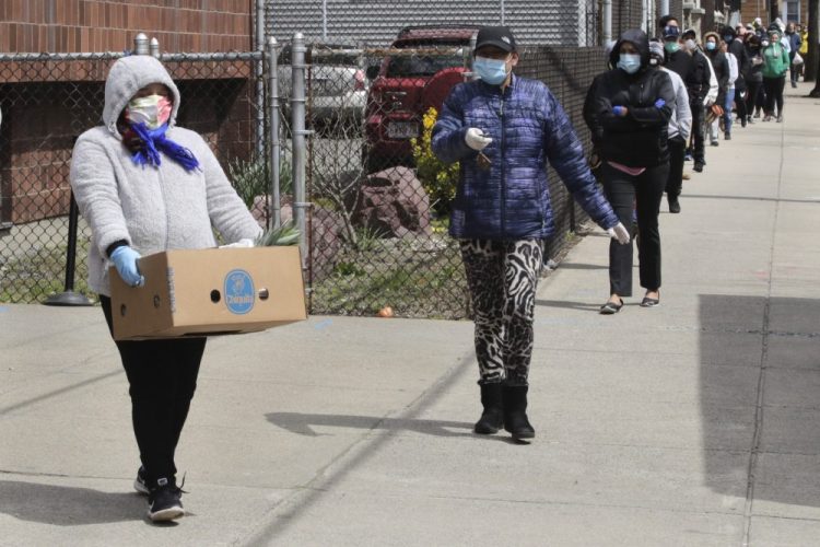 A woman carries a box of food away as hundreds others impacted by the COVID-19 virus outbreak wait in line at a Salvation Army center in Chelsea, Mass., on Wednesday.