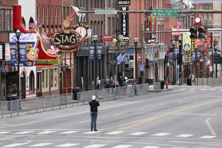 In this March 23, 2020, file photo, a man stands in the middle of Broadway to take a photo where the streets and sidewalks are normally filled in Nashville, Tenn. 