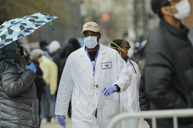A medical worker walks past people lined up at Gotham Health East New York, a COVID-19 testing center, on Thursday in the Brooklyn borough of New York. 