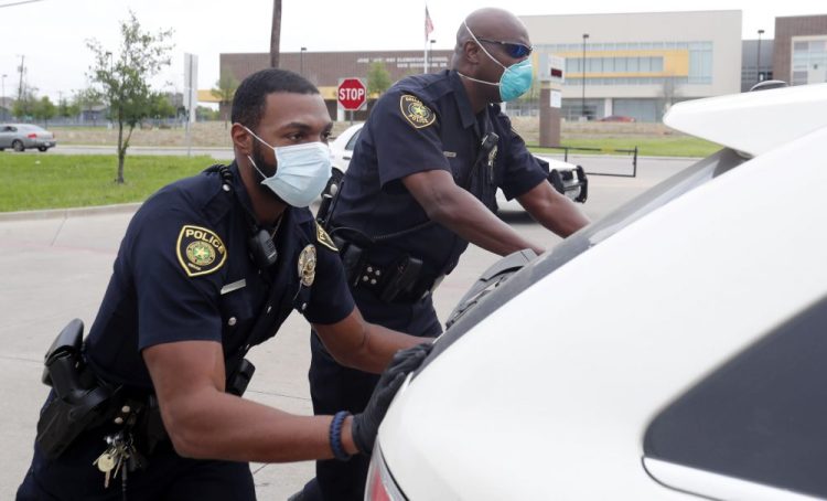 Dallas police officers push a car that ran out of gas while waiting in line for the weekly school meal pick up for students in Dallas. 