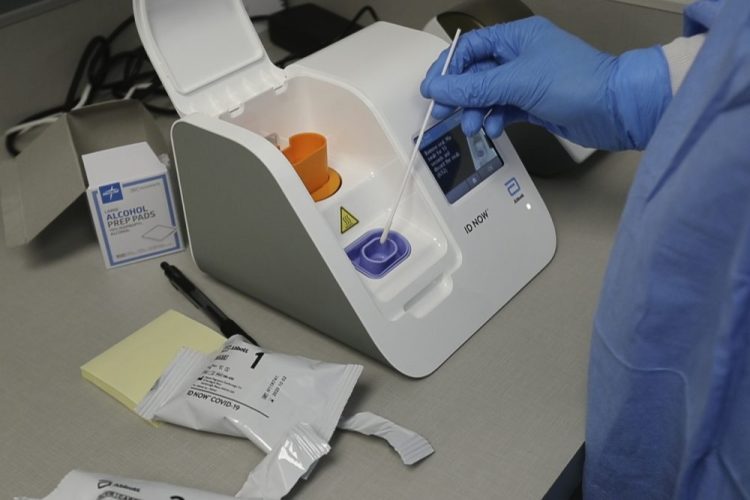 A lab technician dips a sample into the Abbott Laboratories ID Now testing machine at the Detroit Health Center in Detroit on Friday. Illinois-based Abbott Laboratories says its cartridge-based test, approved last month, delivers results within minutes. 
