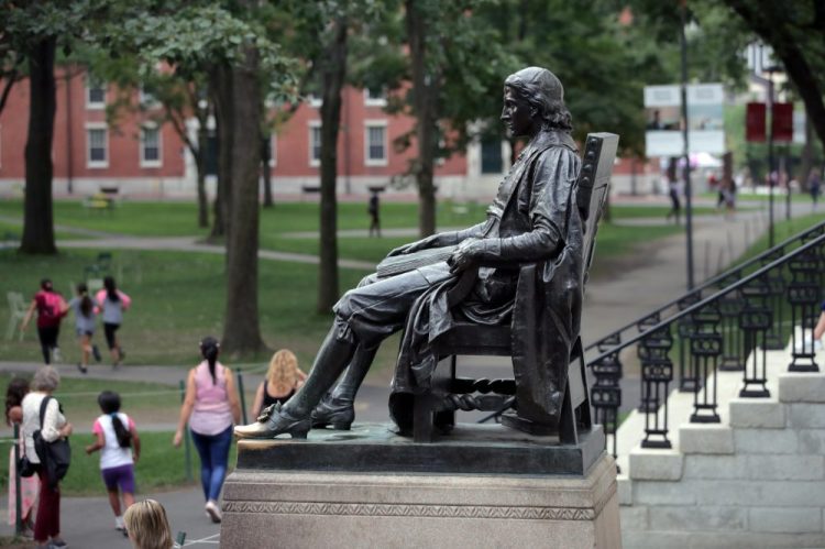 Students walk past the statue of John Harvard at Harvard University on Aug. 13 in Cambridge, Mass.