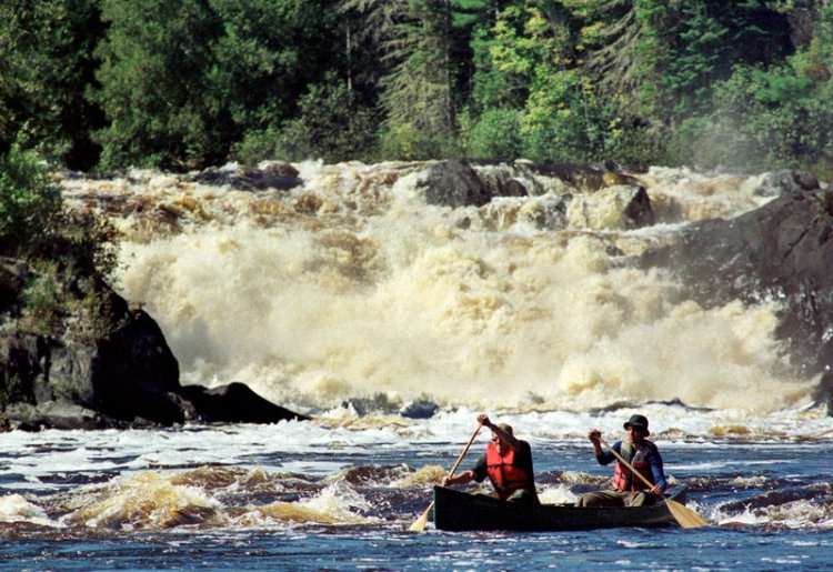 Canoeists Jason Chamberlain, left, and Andrew Martin, both of Fort Kent, Maine, paddle through whitewater after portaging the 40-foot Allagash Falls, background in 1999 on the Allagash Wilderness Waterway 