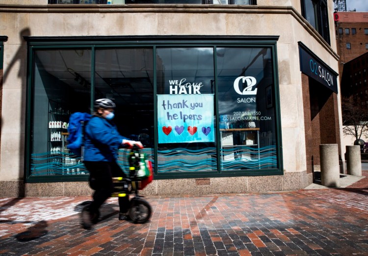A pedestrian passes a sign in the window of a closed salon on Congress Street in Portland on Monday morning.