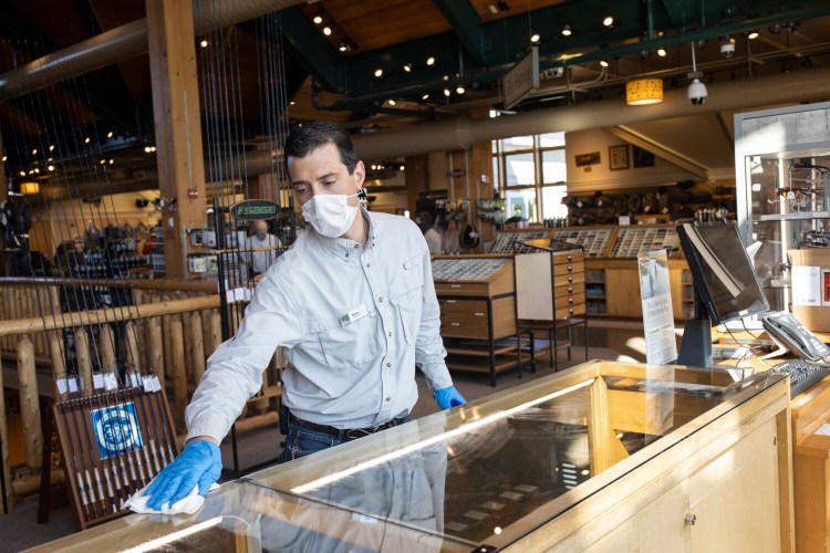 Store manager Ryan Pappas wipes down a display counter at the L.L. Bean Hunting & Fishing store in Freeport on Wednesday. The store was reclassified as essential on March 31 and could have reopened then, but the company chose to keep it closed until this week.
