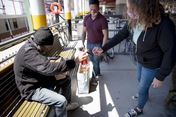 Katie Junkert of The Opportunity Alliance hands a plastic fork to a homeless man at the Maine State Pier in Portland on May 14. Junkert and Ashish Shrestha of Amistad were giving out free meals as part of the Cooking for Community effort. Cooking for Community is one of the programs that will receive grant money from the John T. Gorman Foundation.