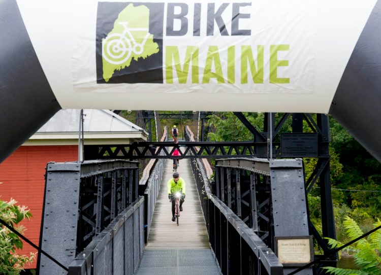 Riders cross the Two Cent Bridge from Winslow as they make it to Head of Falls in Waterville to finish the 2019 BikeMaine weeklong cycling trip around the state. Some 450 riders participate in the annual event.