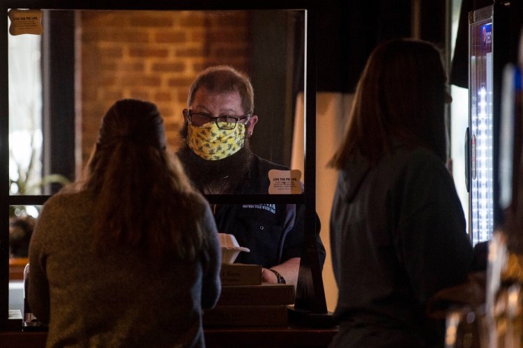 A patron at Portland Pie pays for his to-go order in Waterville on Friday, the day Gov. Janet Mills ordered residents to wear masks in public places where physical distancing is difficult to maintain to prevent the spread of COVID-19.