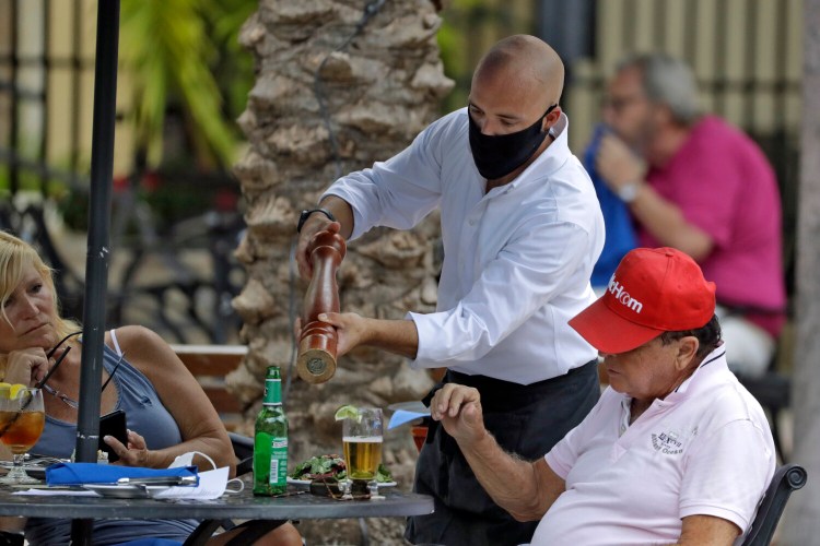 A food server wearing a protective face mask waits on customers Monday at the Parkshore Grill restaurant in St. Petersburg, Fla. Several Florida restaurants are reopening at 25 percent capacity as part of  Gov. Ron DeSantis' plan to stop the spread of the coronavirus. 