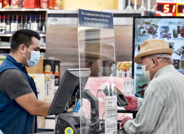 A grocery worker, wearing a protective mask and gloves, helps check out a customer  at the 99 Ranch Market on Tuesday in Los Angeles.