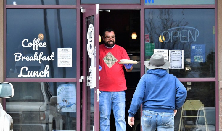 Jesse Arellano hands a breakfast burrito to his friend and regular, Robert Taylor, from the front door of his restaurant, C&C Breakfast and Korean Kitchen, in Castle Rock, Colo., on Monday. Arellano and his wife, April Arellano, opened their restaurant for Mother's Day and had a packed restaurant at times Sunday. When video from the scene went viral, the Arellanos received both backlash and support. The restaurant was ordered to close Monday and had its license suspended indefinitely by health officials. 