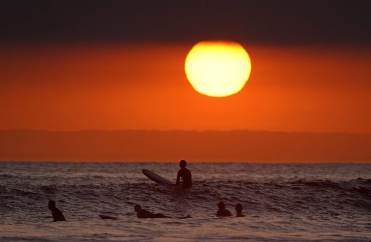 Surfers wait for waves as the sun goes down the day before the beach is scheduled to close during the coronavirus outbreak, Thursday in Newport Beach, Calif. California Gov. Gavin Newsom on Thursday temporarily closed Orange County's coastline after large crowds were seen there.
