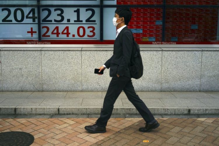 A man wearing a face mask walks past an electronic stock board showing Japan's Nikkei 225 index at a securities firm in Tokyo on Monday. 