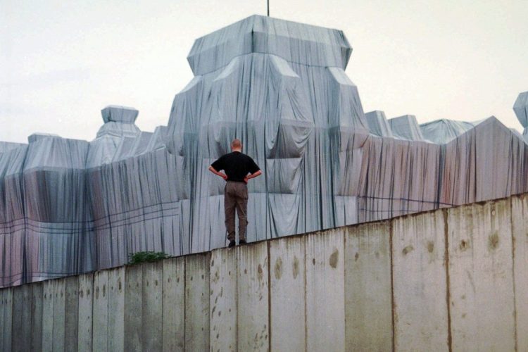 A man stands at the top of remains of the Berlin Wall and looks at the wrapped Reichstag building, a project titled "Wrapped Reichstag" by American artist Christo and his wife Jeanne-Claude in 1995. 