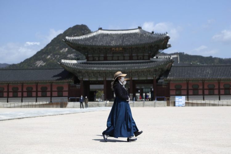 Masked women walk past the Gyeongbok Palace, in Seoul, South Korea. Nervous travelers, spotty air service, health risks –  the battered global tourism industry is facing unprecedented uncertainty in the wake of the new coronavirus. 