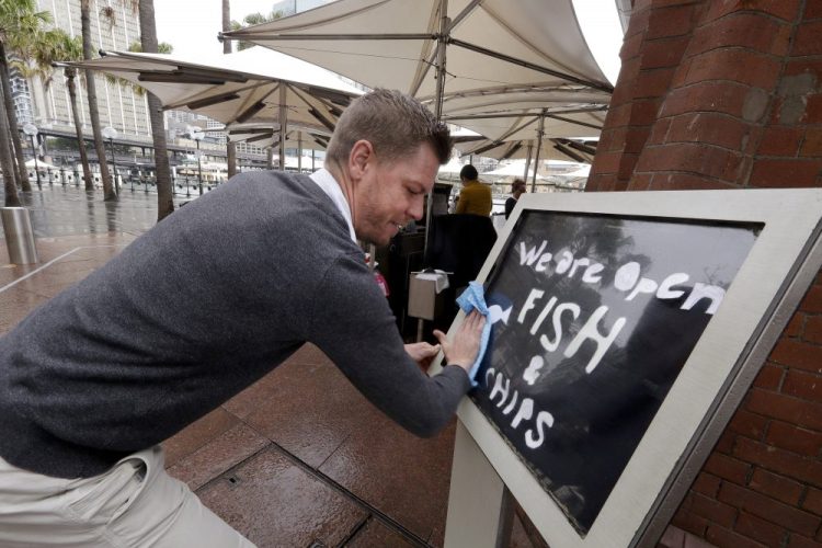 Alec Owes wipes a sign alerting customers that the Sydney Cove Oyster Bar is open as stage 1 of the lifting of COVID-19 restrictions begin in Sydney. Some pubs, clubs and restaurants are reopening with a limit of 10 patrons while following distancing guidelines.