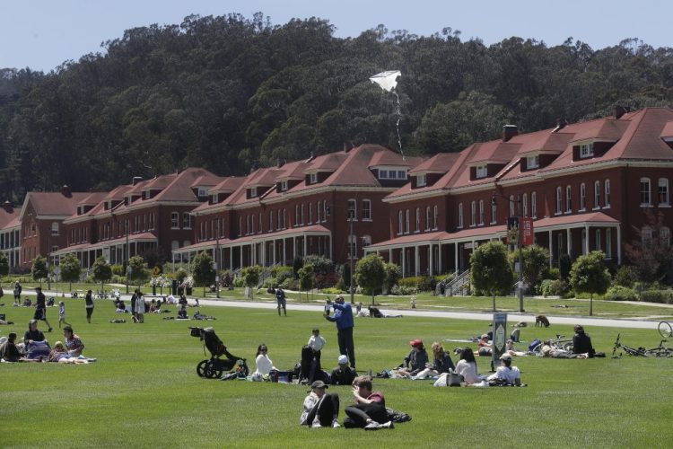People sit and fly kites on grass in The Presidio, part of the Golden Gate National Recreation Area in San Francisco on Sunday. 
