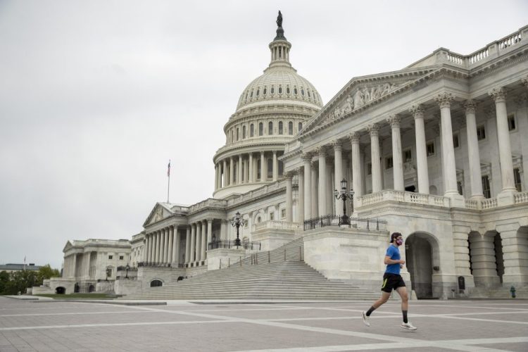 A man wearing a mask depicting American flags jogs past the U.S. Capitol Building, Tuesday, April 28.