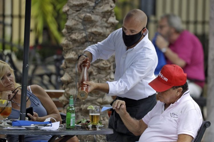 A food server wearing a protective face mask waits on customers at the Parkshore Grill restaurant Monday, May 4, 2020, in St. Petersburg, Fla. 