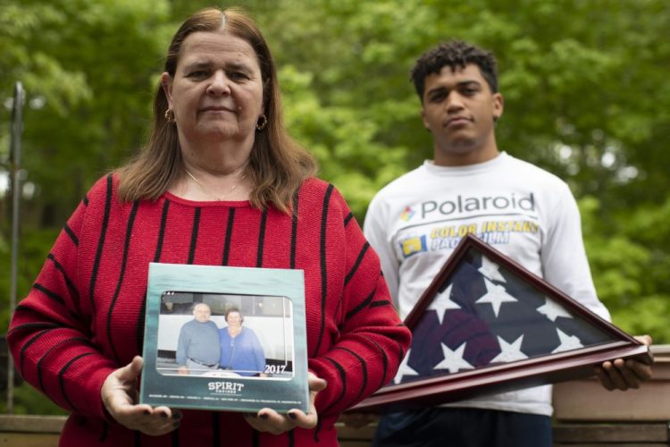 Florence Hopp, left, holds a photograph of herself and her husband Robert Hopp during a cruise in 2017, as her son J.J. Brania-Hopp holds the American flag the military presented to them after his father's death at their home in Boonton, N.J. Robert Hopp was one of at least 79 residents of a veterans home in Paramus, N.J., to die from COVID-19. 
