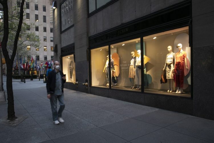 A man wearing a mask walks by a window display at a J Crew store in Rockefeller Center, Saturday in New York. The company announced it would apply for bankruptcy protection amidst the COVID-19 pandemic.  