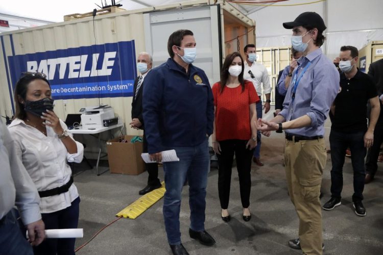 Florida Gov. Ron DeSantis, center, tours decontamination units at a COVID-19 testing site with Sean Harrington of Battelle Critical Care Decontamination System, right, at Hard Rock Stadium on Wednesday in Miami Gardens.