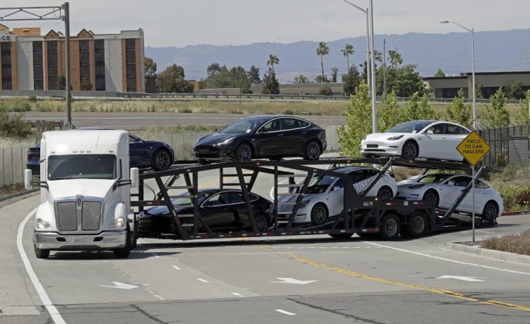 A truck hauling new Tesla vehicles leaves the Tesla factory plant on Monday in Fremont, Calif. Two workers, who spoke on the condition of anonymity because they feared for their jobs, said they were concerned about the sudden escalation of production. One said employees were working without face masks. 